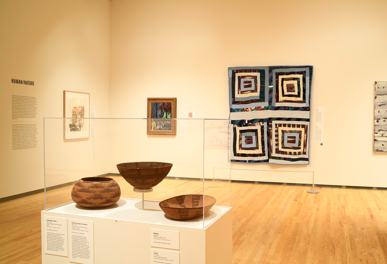 An installation shot of "Generations," featuring pottery, a print, a painting, and a quilt