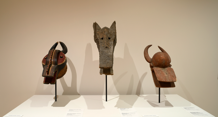 An installation shot of three zoomorphic masks on a pedestal in the installation "About Face."