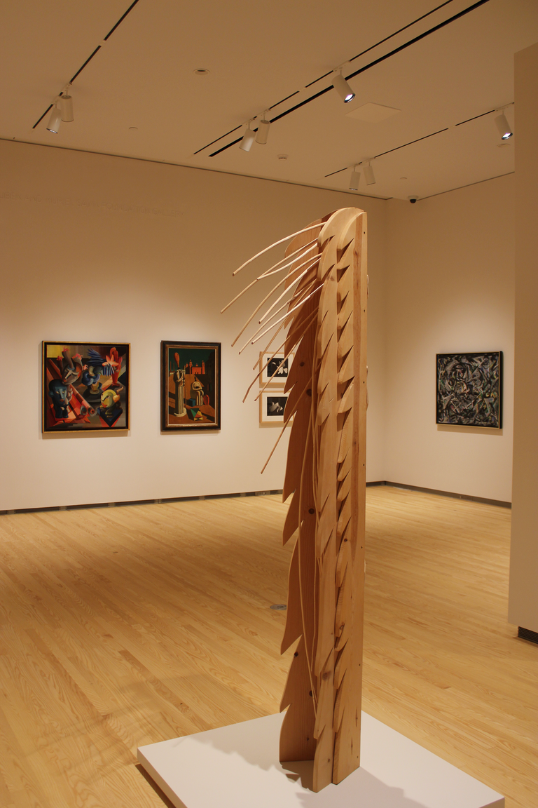 An installation shot of the galleries: a tall sculpture is at the foreground, with four paintings visible in the background.