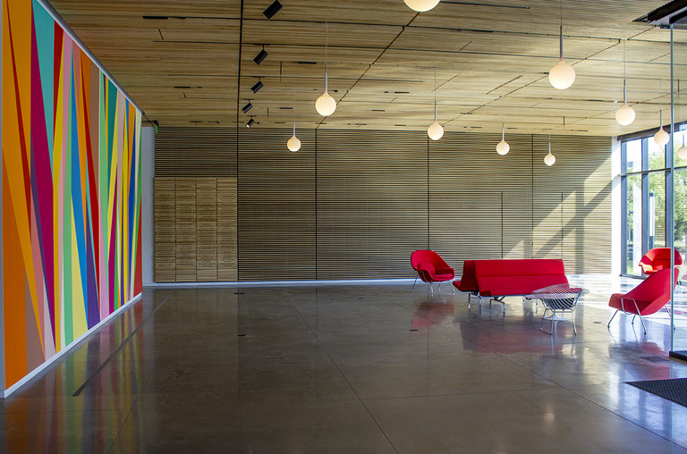 A long lobby with cement floors, red lounge chairs, dropped lighting fixtures, and natural light.
