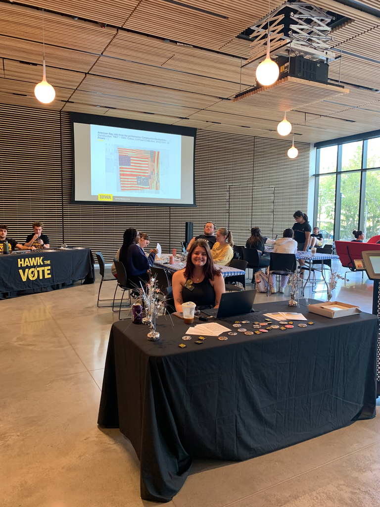 A photo of the Art of Voting event, showcasing the info table at the front of the event. At the table sits Campus Engage Coordinator Alexis Belme, who is smiling, prepared to greet event attendees as they walk through the museum's front doors.