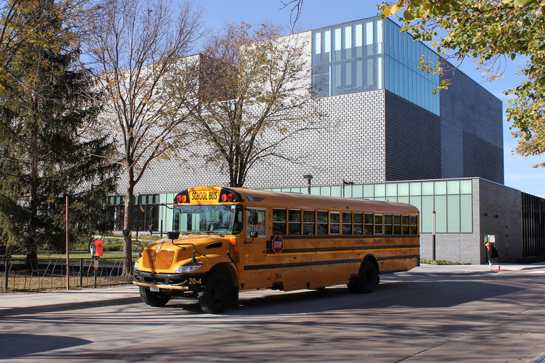 Yellow school bus parked in front of a grey brick building with large windows at the top corner