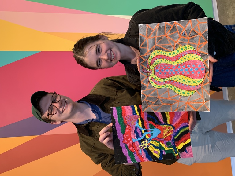 two students standing in front of the lobby mural holding their finished products 