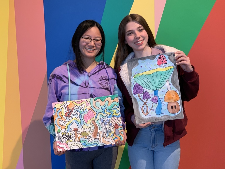 two students standing in front of the mural showing their finished products 