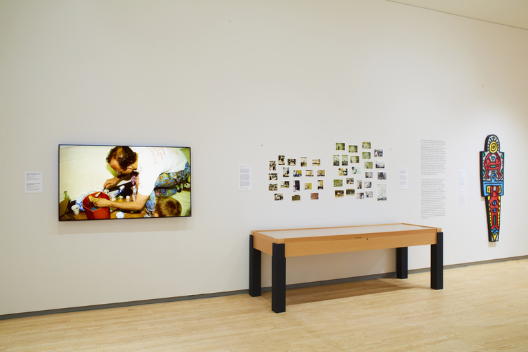 Gallery wall with a screen, photographs and a colorful wooden totem on display