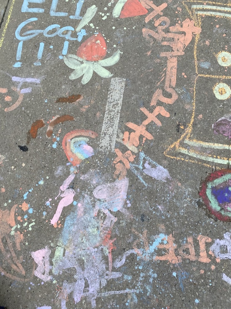 A photo of the ground with sidewalk chalk drawings, featuring outlines drawn of people that resemble Keith Haring-style figures. 