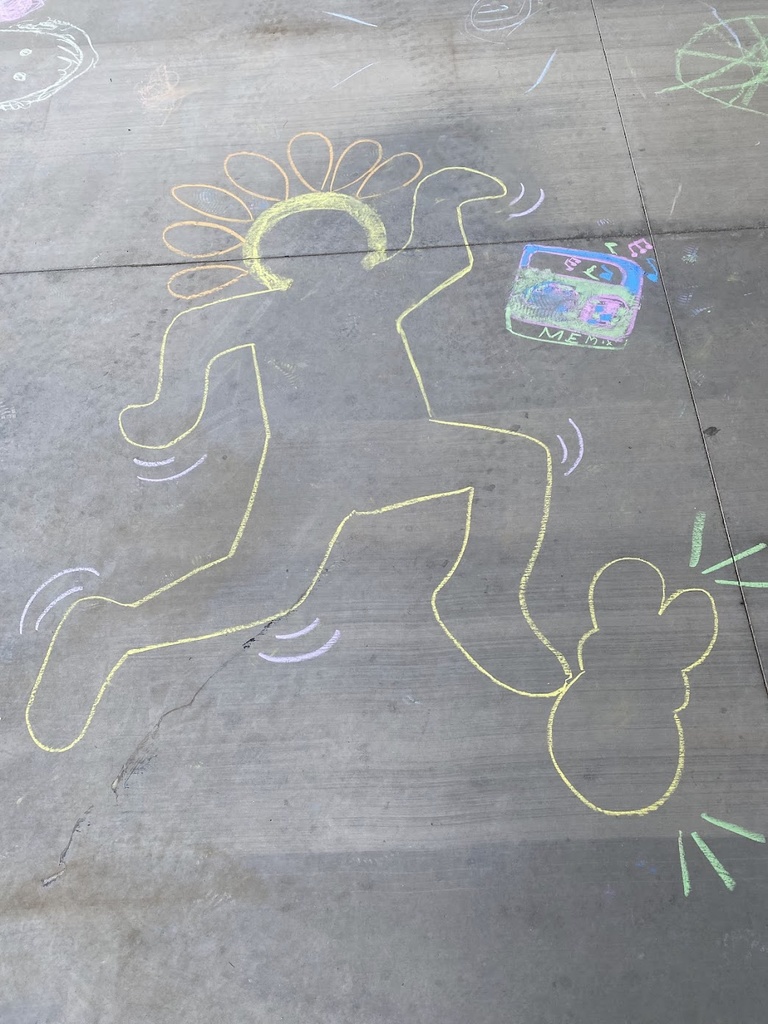 A photo of the ground with sidewalk chalk drawings, featuring outlines drawn of people that resemble Keith Haring-style figures. 