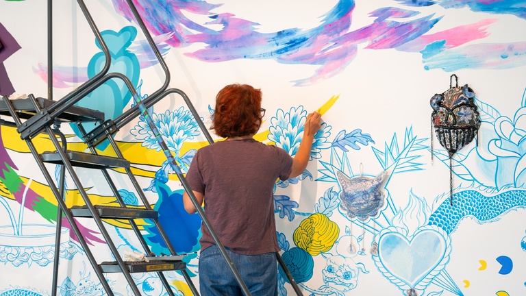 A person on a ladder painting designs on a wall
