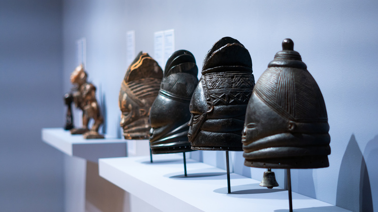 A series of masks on display in a gallery with purple walls