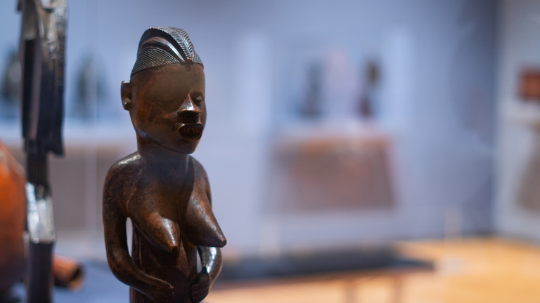 A wooden female figure on display in a gallery 