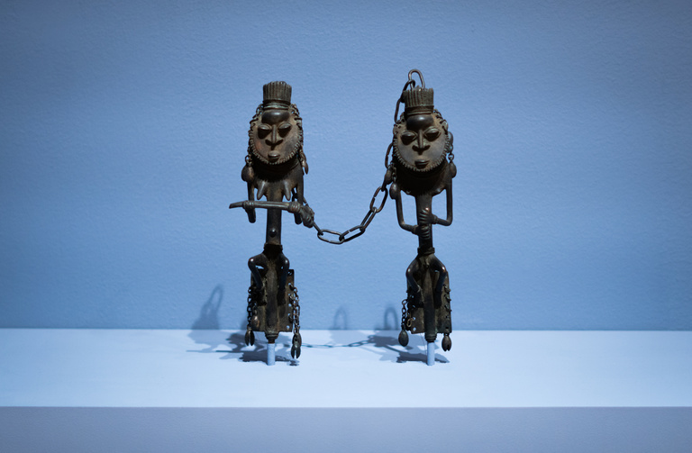 Two brass figures connected by a chain on display in a gallery