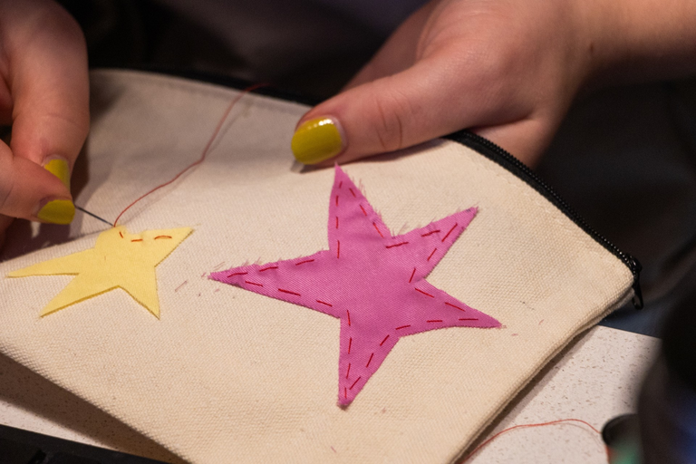 A close up on one student's project: a white canvas pencil case that has had patchwork stars in yellow and pink applied.