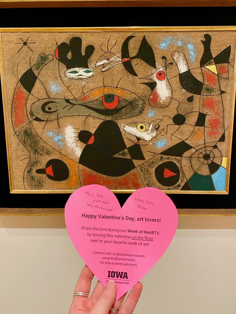 A hand holding a heart in front of a Miro painting.