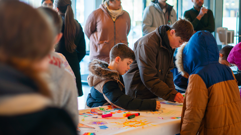 A group of mixed children and adults work on and watch others work on the murals.