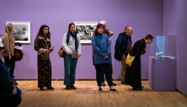 A group of visitors observing photographs displayed on purple walls in an art museum 