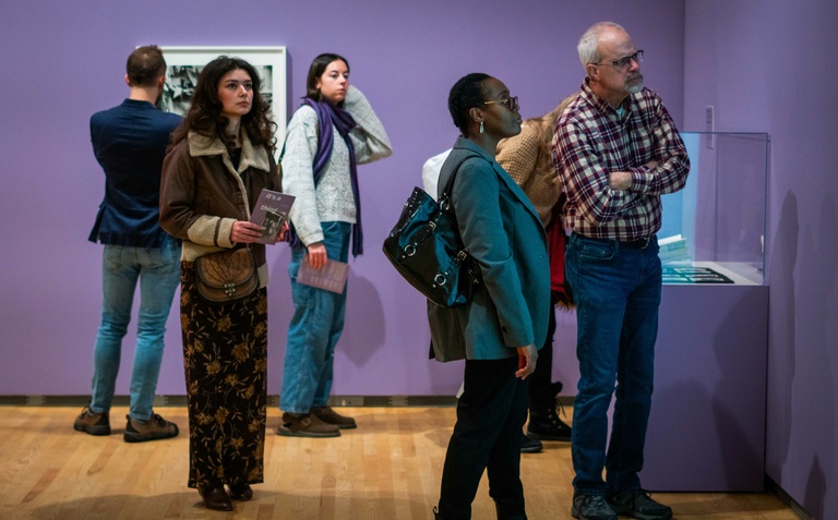 A group of visitors observing photographs displayed on purple walls in an art museum 