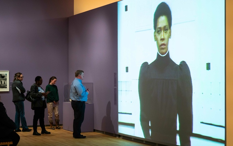 A group of visitors observing a large video projection on a wall in an art museum 