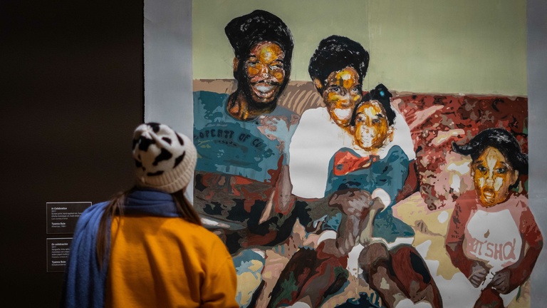 A person views a large colorful painting of a black family displayed in a museum