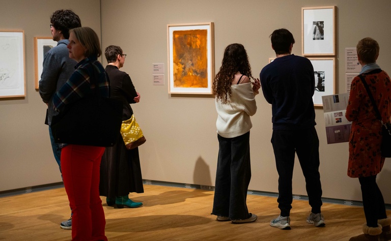 A group of visitors observing artworks displayed on walls in an art museum 