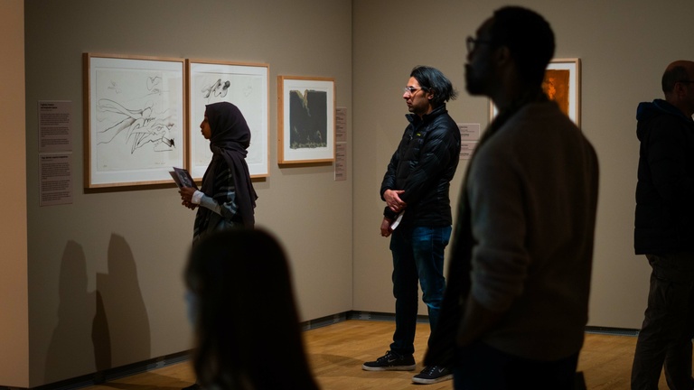 A group of visitors observing artworks displayed on walls in an art museum 