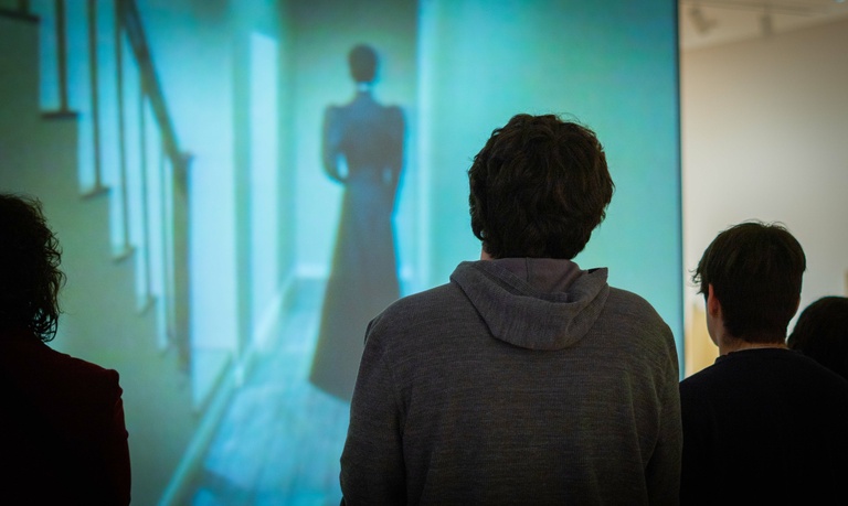 Visitors observe a video projection playing on the wall of an art museum