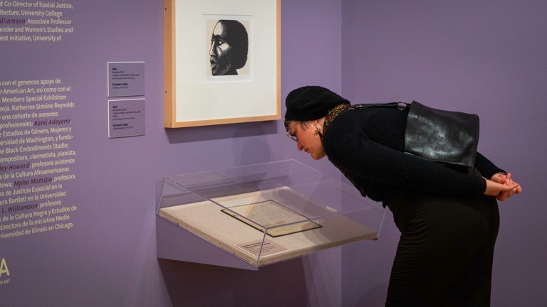 A person in a black dress leans forward to look at an object on display in a glass case.