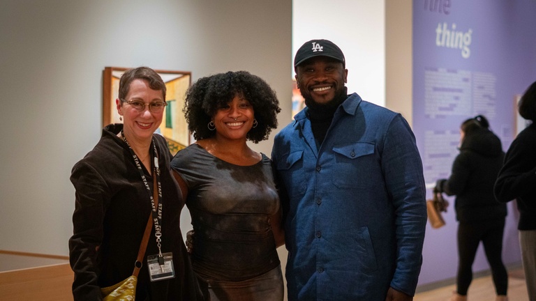 A group of three people in a gallery standing together posing for a photograph, smiling