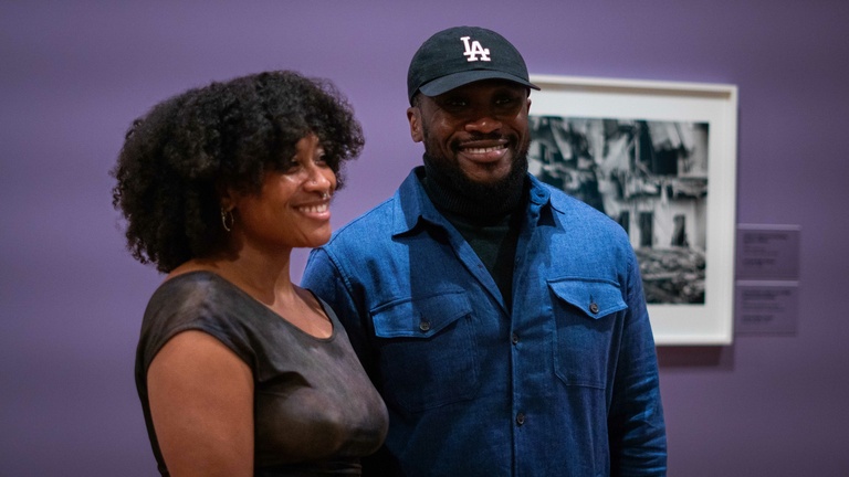 Two people standing in a gallery with purple walls, posing for a photograph, smiling