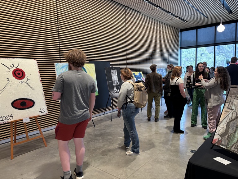 A group of people explore artworks on display at the 2025 Student Exhibit.