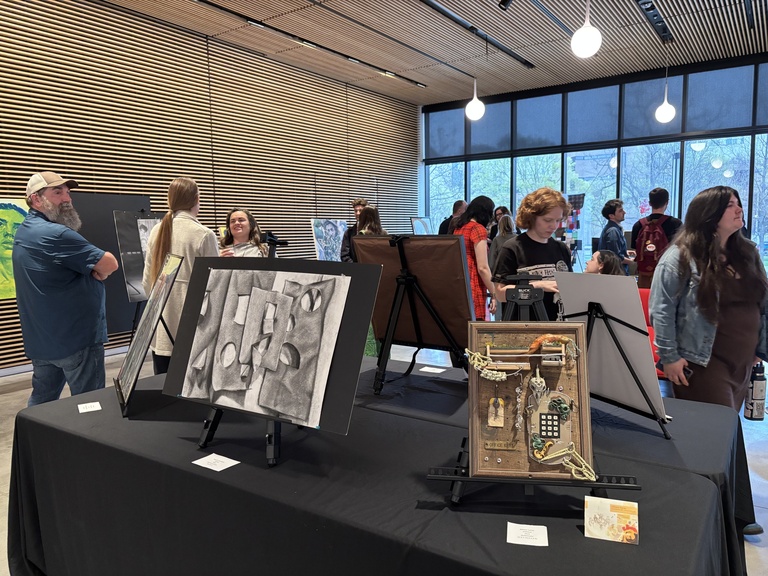 A group of people explore artworks on display at the 2025 Student Exhibit.