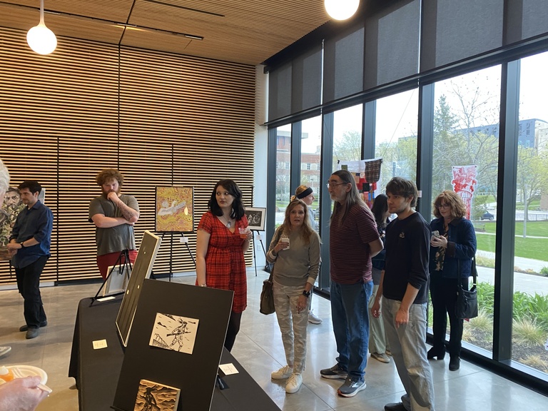 A group of people explore artworks on display at the 2025 Student Exhibit.