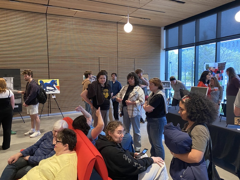 A group of people explore artworks on display at the 2025 Student Exhibit.