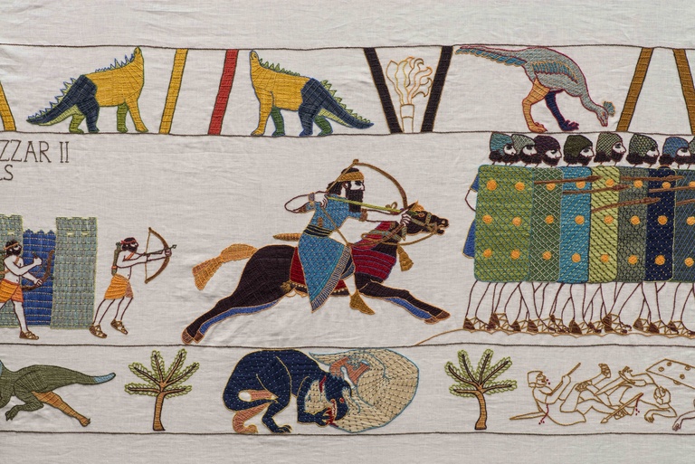 Embroidered tapestry depicting warriors in battle, archers, soldiers with shields, horses, palm trees, and dinosaurs in the style of the Bayeux Tapestry.