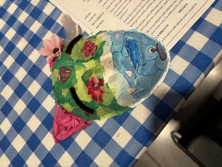 One student's mask, featuring blue and green tissue paper, pink flowers, and pink ears.