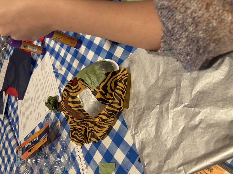 A student working on their mask, which currently has animal print tissue paper all over it.