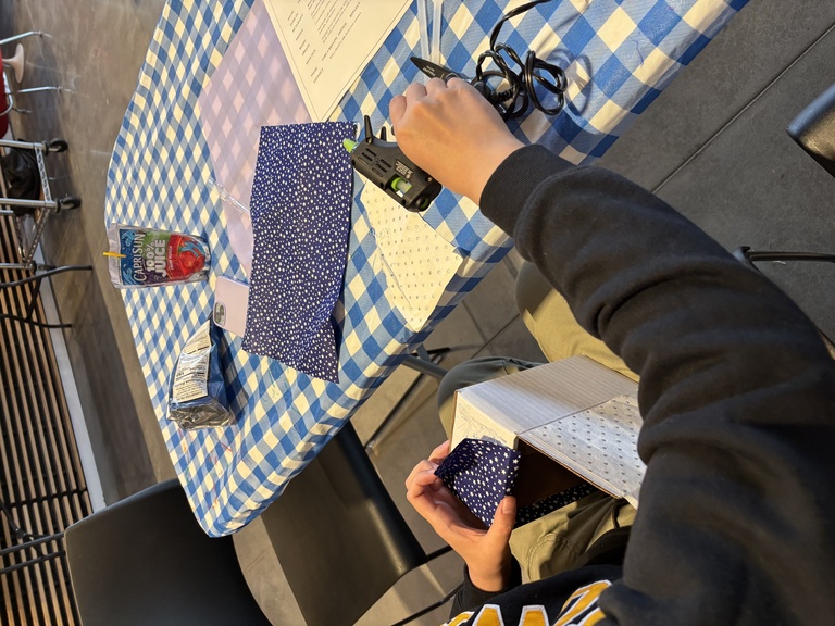 A student holds a glue gun and attached paper to their story box.