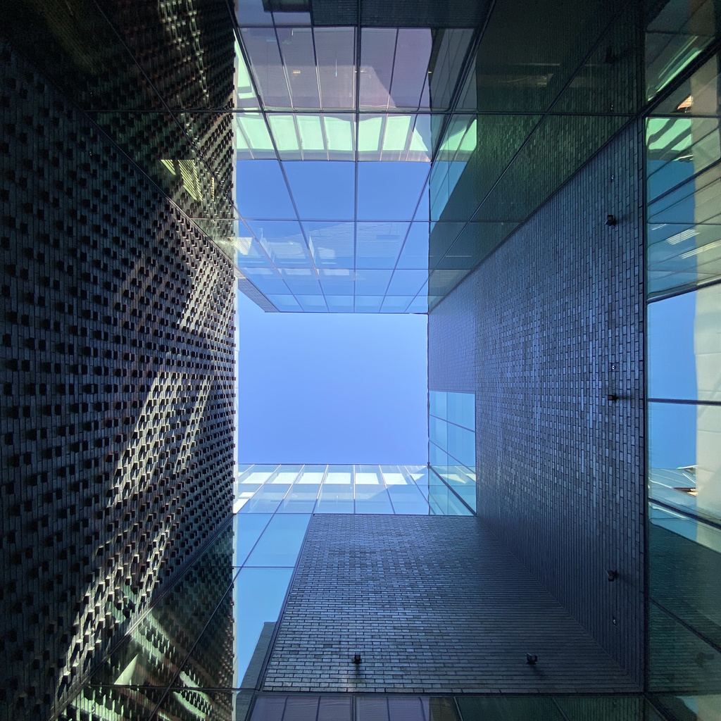 Looking up the lightwell past brick and glass walls toward a square of blue sky.