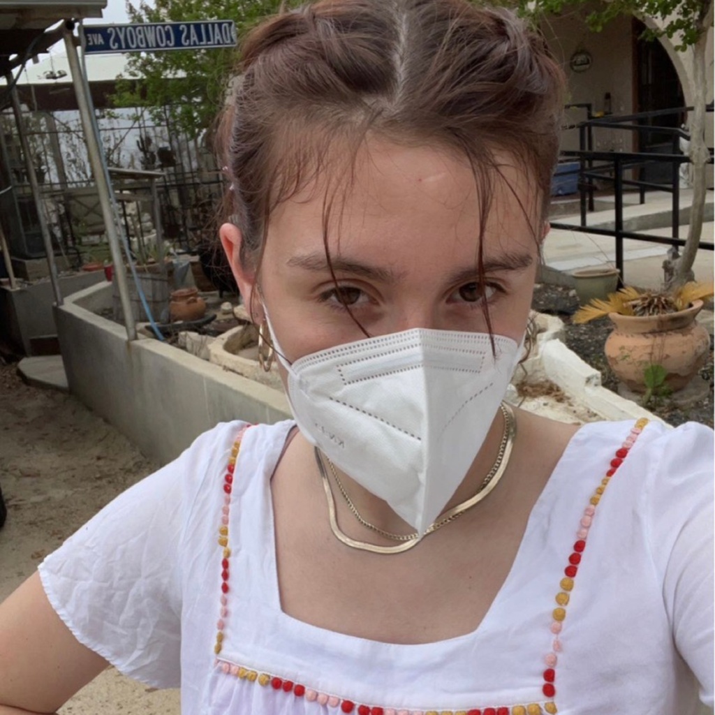 A photo of Erin Elizalde: she is facing the camera, hand on her hip, a KN95 mask covering the bottom half of her face.