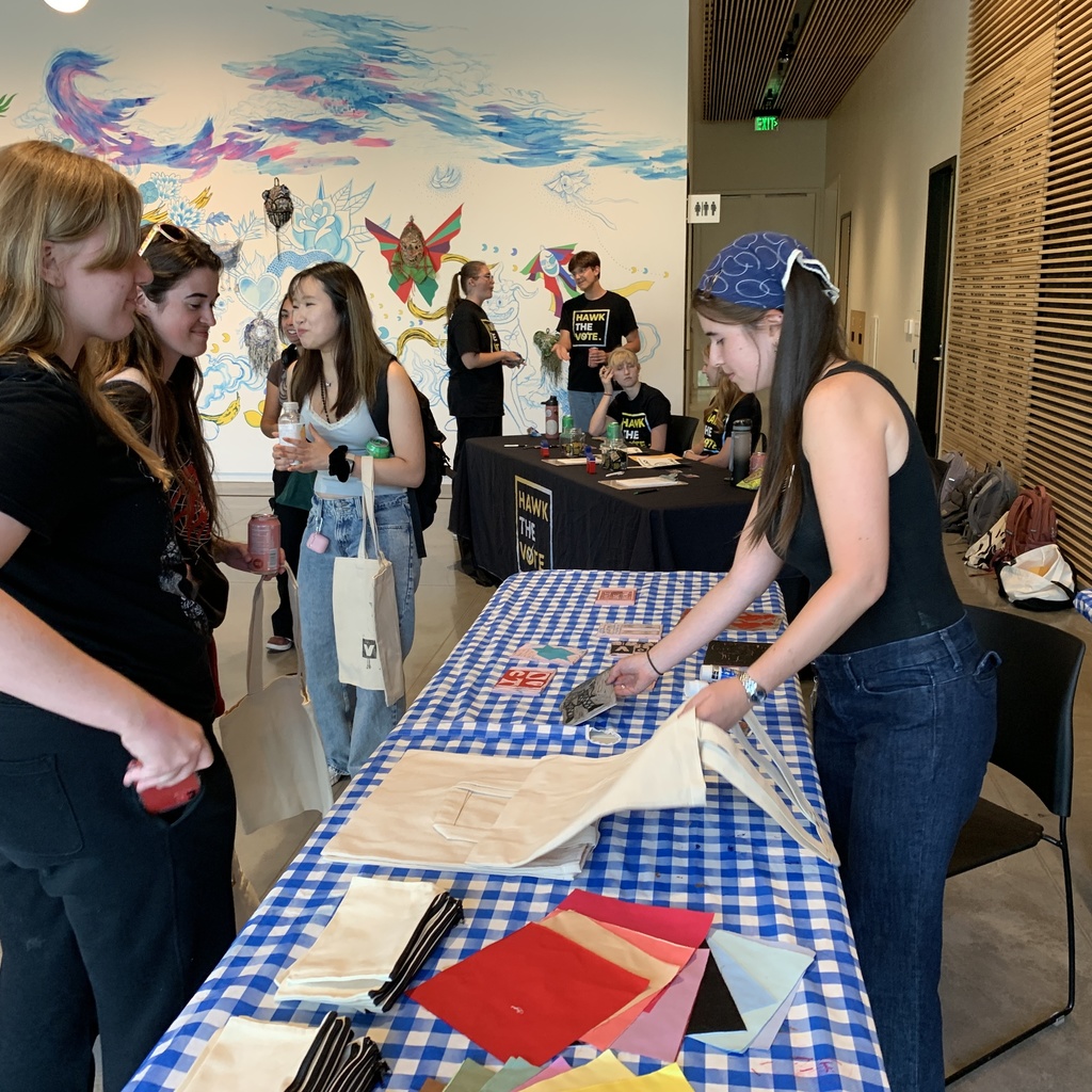 Students wait and watch as Annelies block prints voting-inspired imagery onto tote bags, pencil cases, fabric patches, or other fabric items at the direction of the students.