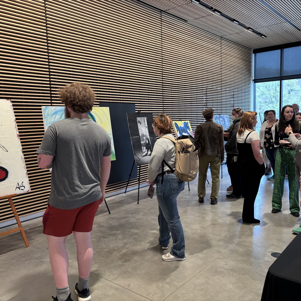 A group of people explore artworks on display at the 2025 Student Exhibit.