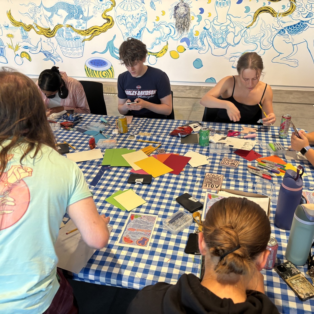 Students sit around a table, carving linoleum blocks to make stamps.