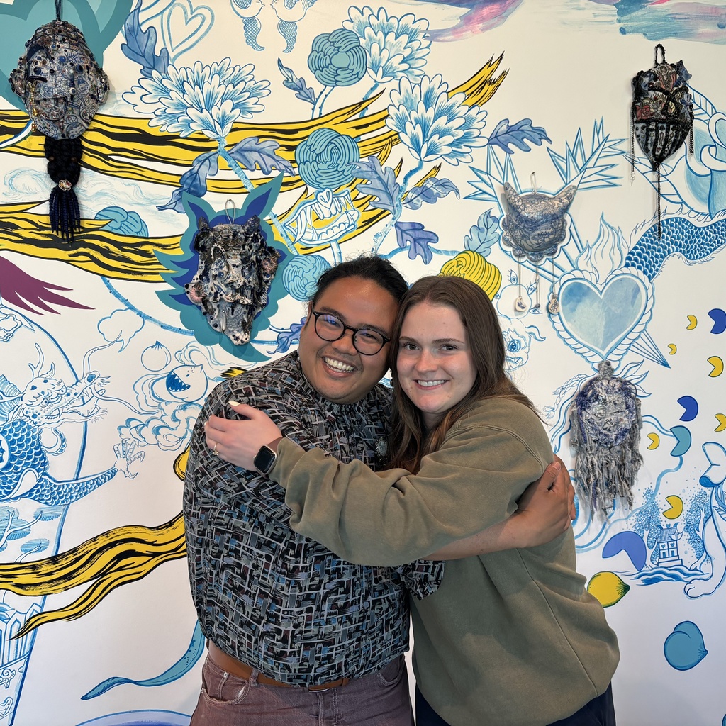 Shaun and Amelia hug each other, posing in front of the Jiha Moon mural in the museum lobby
