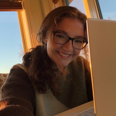 A photo of Emalie Brannigan: she is posing, half hidden by her laptop screen, smiling down at the camera.