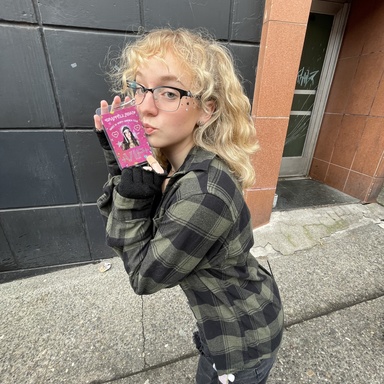 A photo of Julia Culbertson: she is posing with a VIP concert pass in front of a brick building.