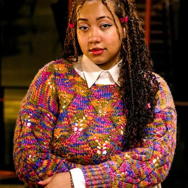 A photo of Lily Hester: they are posing in Art Building West, wearing a very colorful sweater.