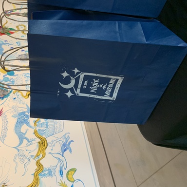 A photo of one of the take and make bags from the October 2024 Night at the Museum event, shown from an angle with the Stanley Museum of Art mural by Jiha Moon in the background.