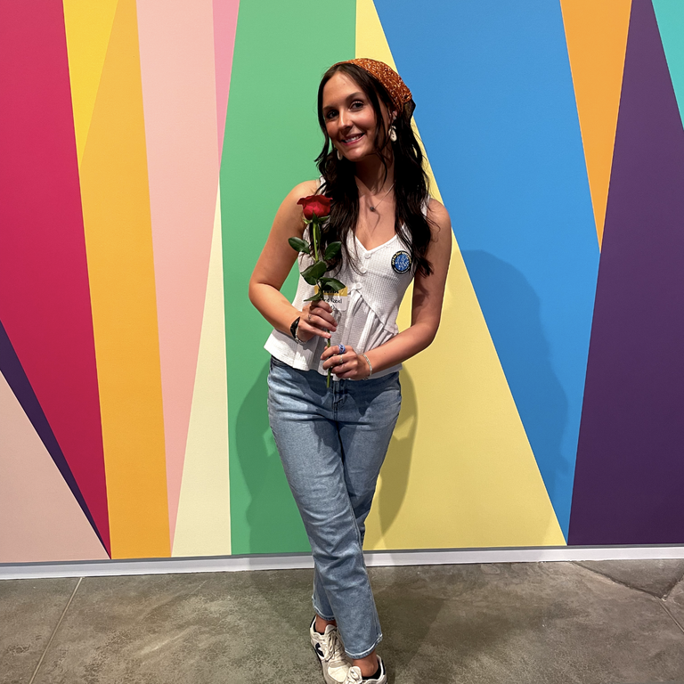 A photo of featured artist Aubrie in front of the mural in the Stanley lobby.