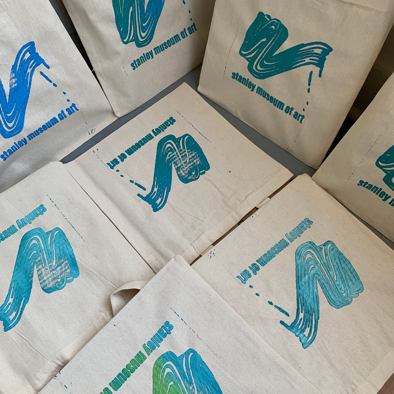 Eight tote bags fill the photograph--they are laid out along the floor to dry, all in different but similar shades and mixes of blue, green, and turquoise.