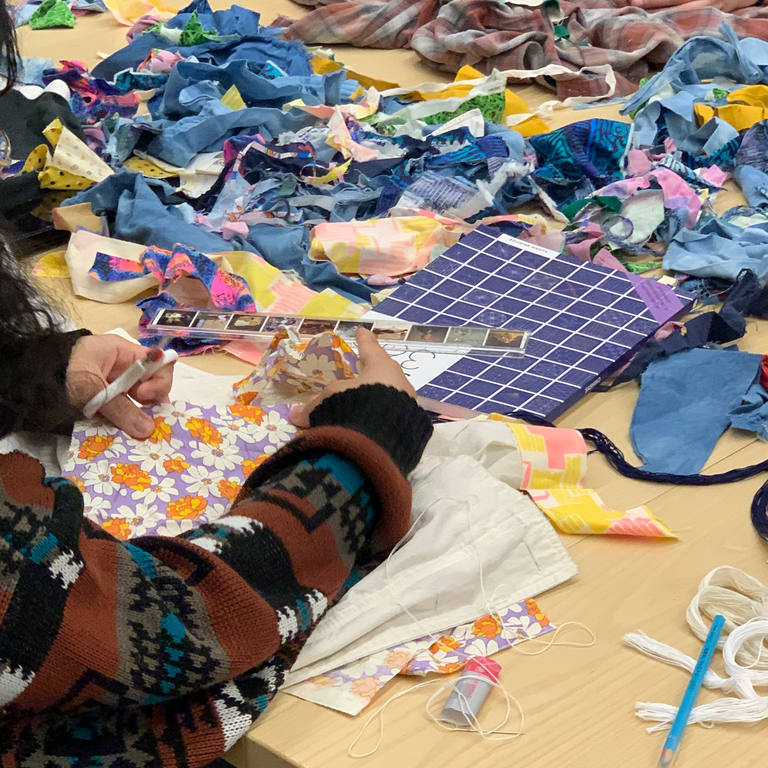An image of the chaos of the work table - books, threads, garments, and colorful piles of scrap fabric in every shape and size.