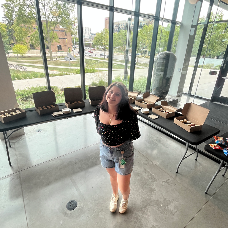 A photo of Alexis, the Stanley's Campus Engagement Coordinator and the student in charge of the HBD event, posing in front of the tables with the cupcakes on them.